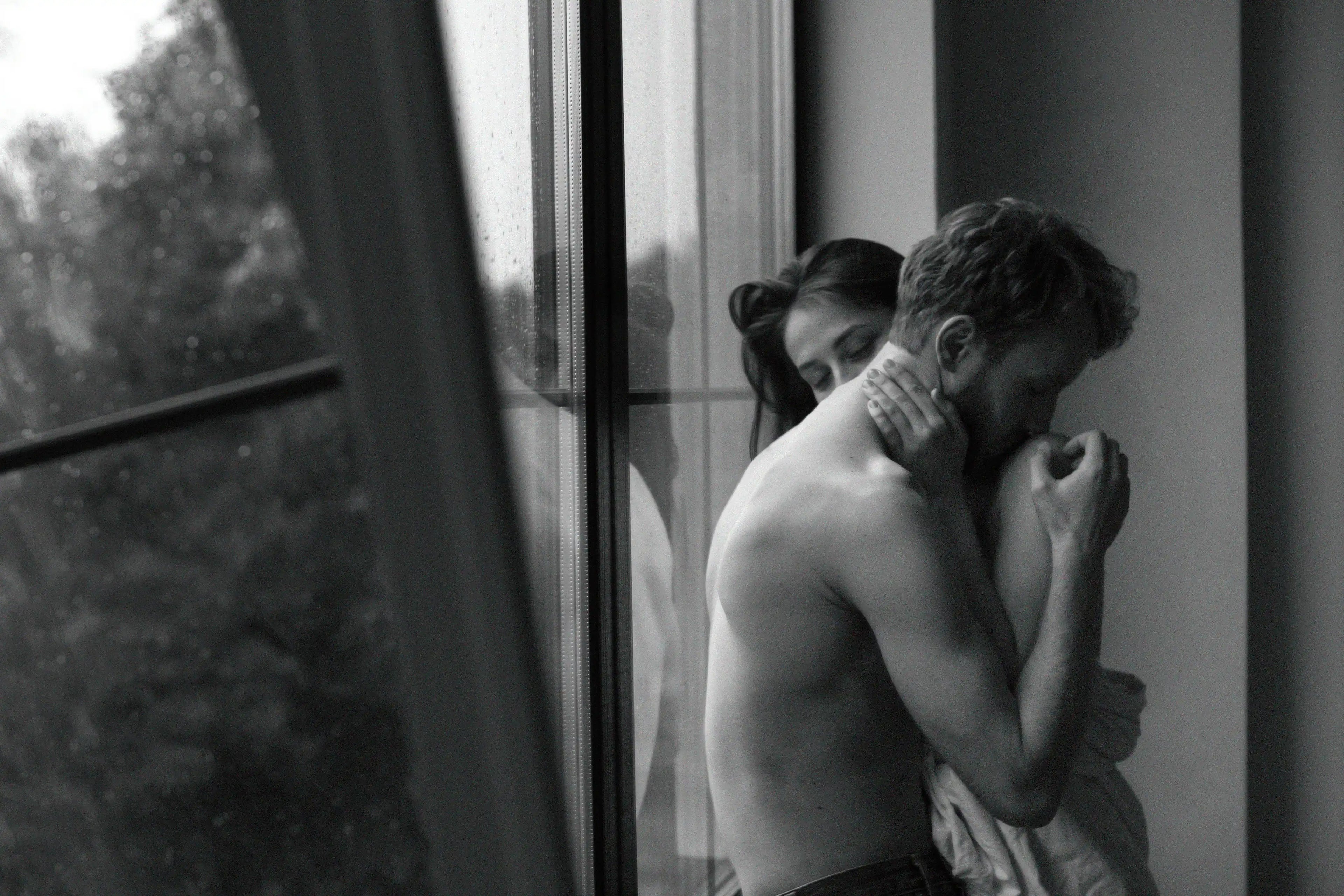 Two people embracing by a window with a blurred outdoor view